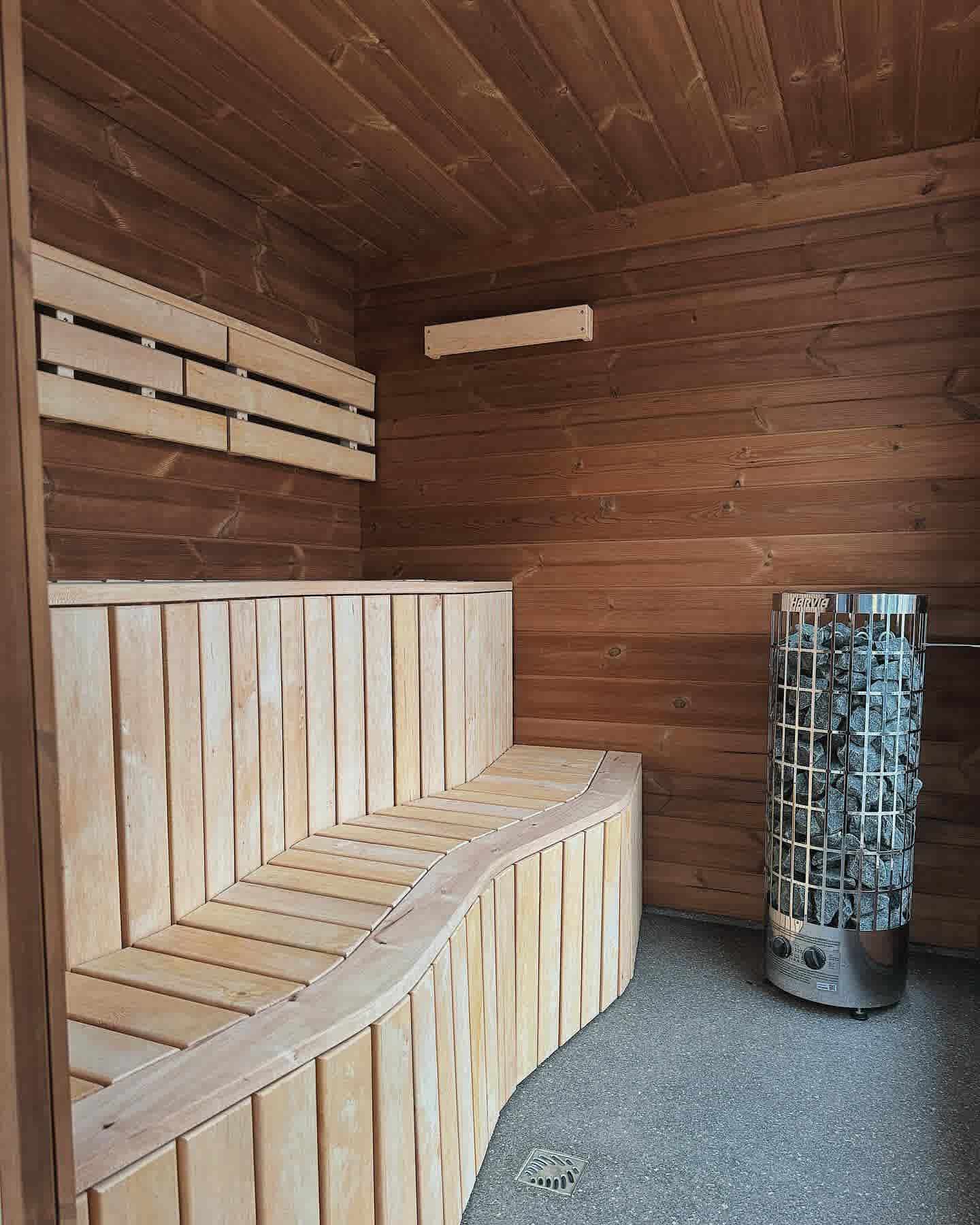 Interior of a modern cube sauna featuring curved ergonomic timber seating and a Harvia electric heater