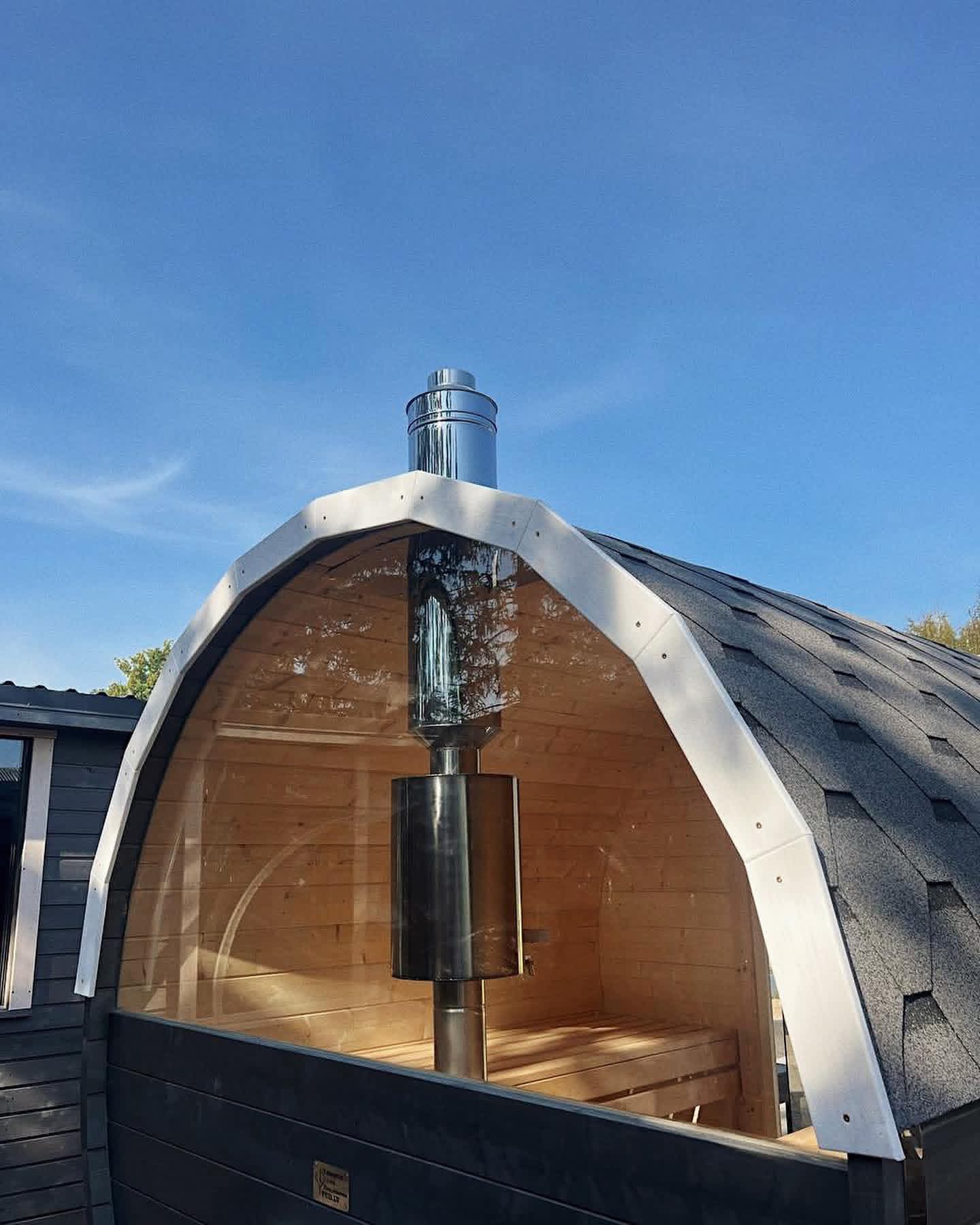 Rear view of a barrel sauna showing the stainless steel chimney for a wood-fired heater and panoramic window.