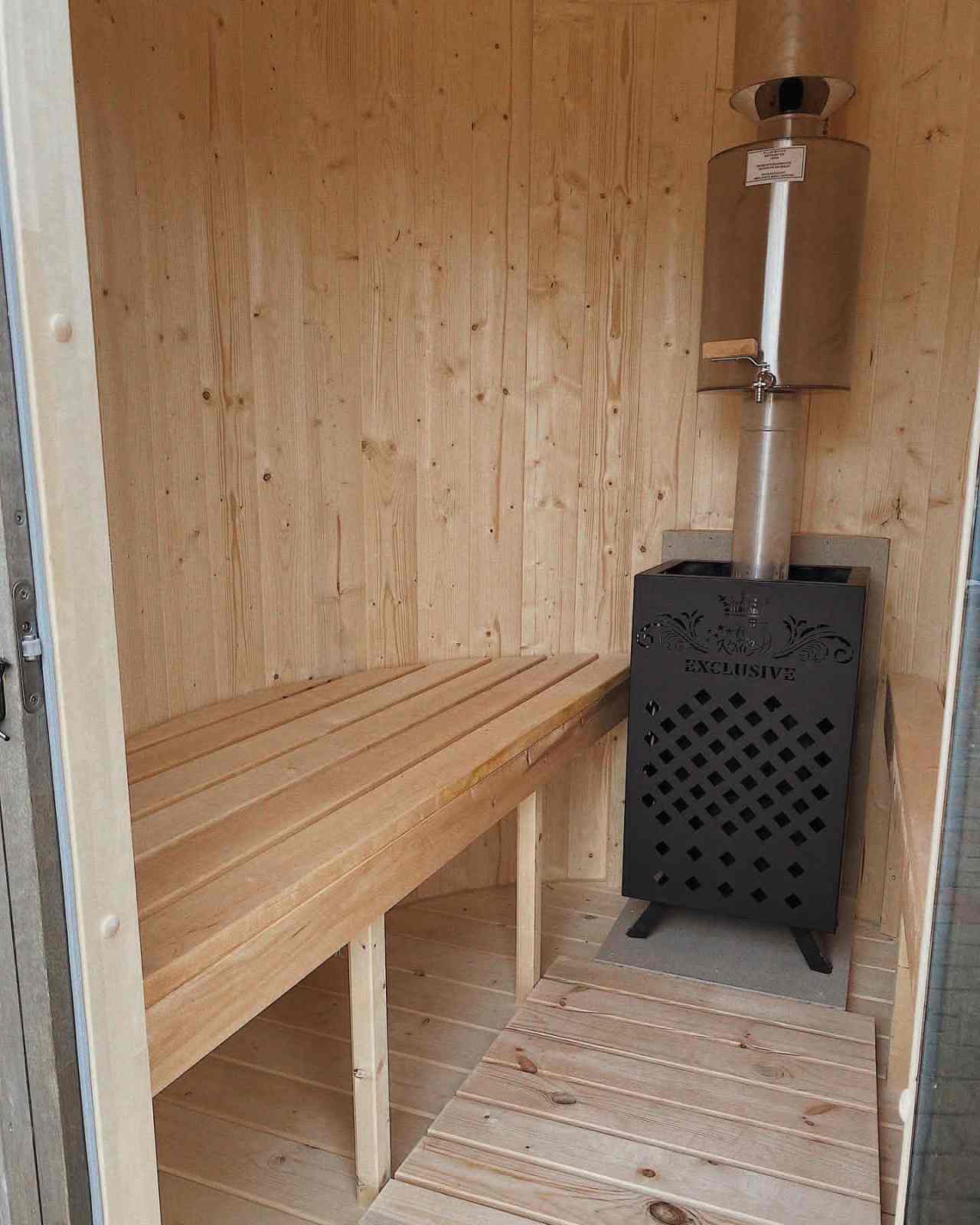 Wide-angle shot of clean sauna bench lines and a high-efficiency wood-fired heater with chimney.