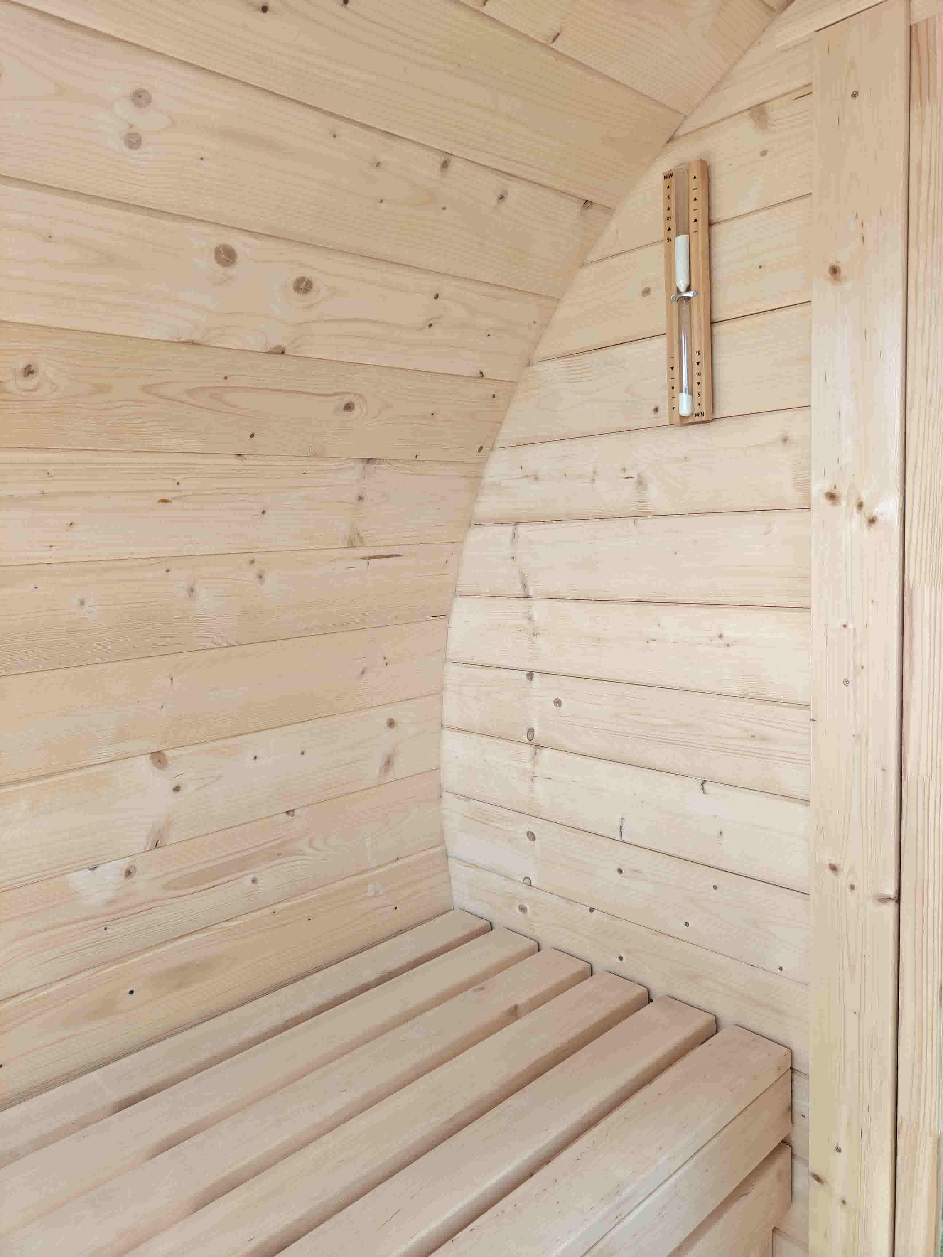 The Cadus interior of a Terra Sauna barrel sauna in Guernsey, featuring curved walls made of kiln-dried spruce and handcrafted smooth alder benches, with a traditional sand timer mounted nearby.