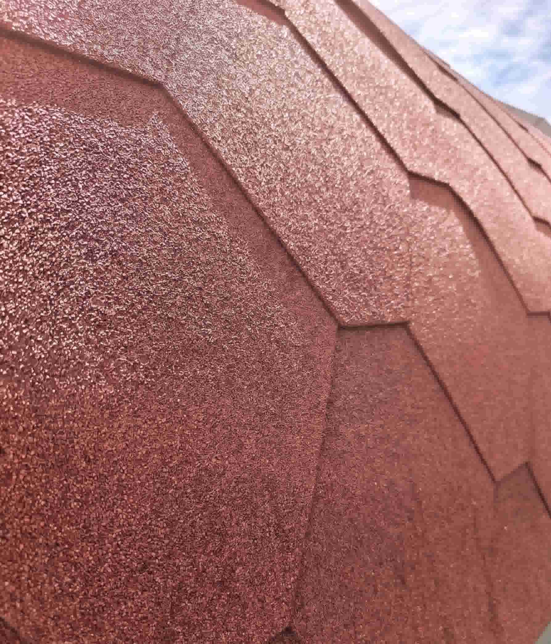 A close-up shot of terracotta red bitumen roofing shingles on a Terra Sauna structure in Guernsey, displaying the rich earthy color, coarse protective texture, and hexagonal shingle layout.