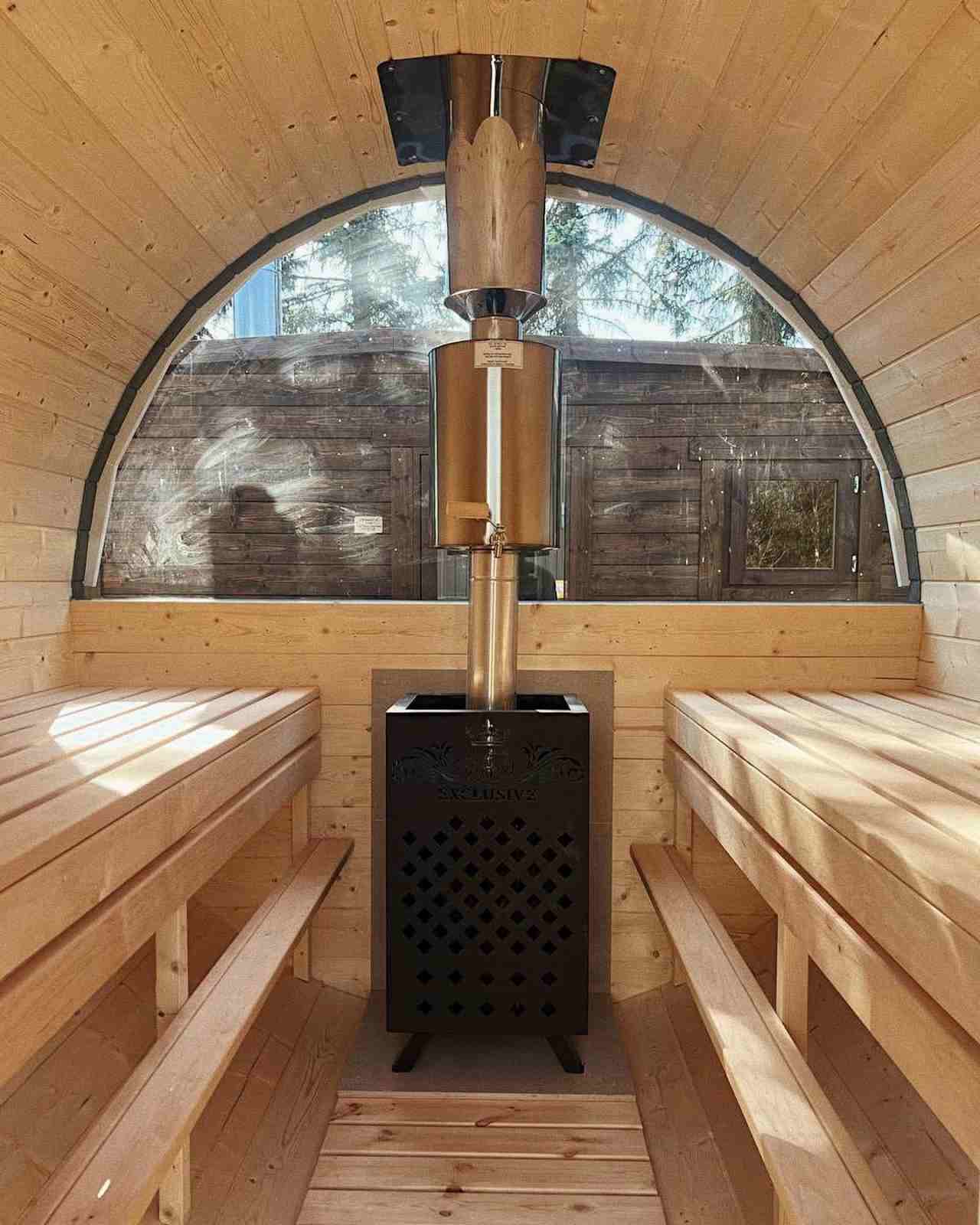 Interior of The Cadus barrel sauna featuring a wood-burning stove and a large semi-circle panoramic window.