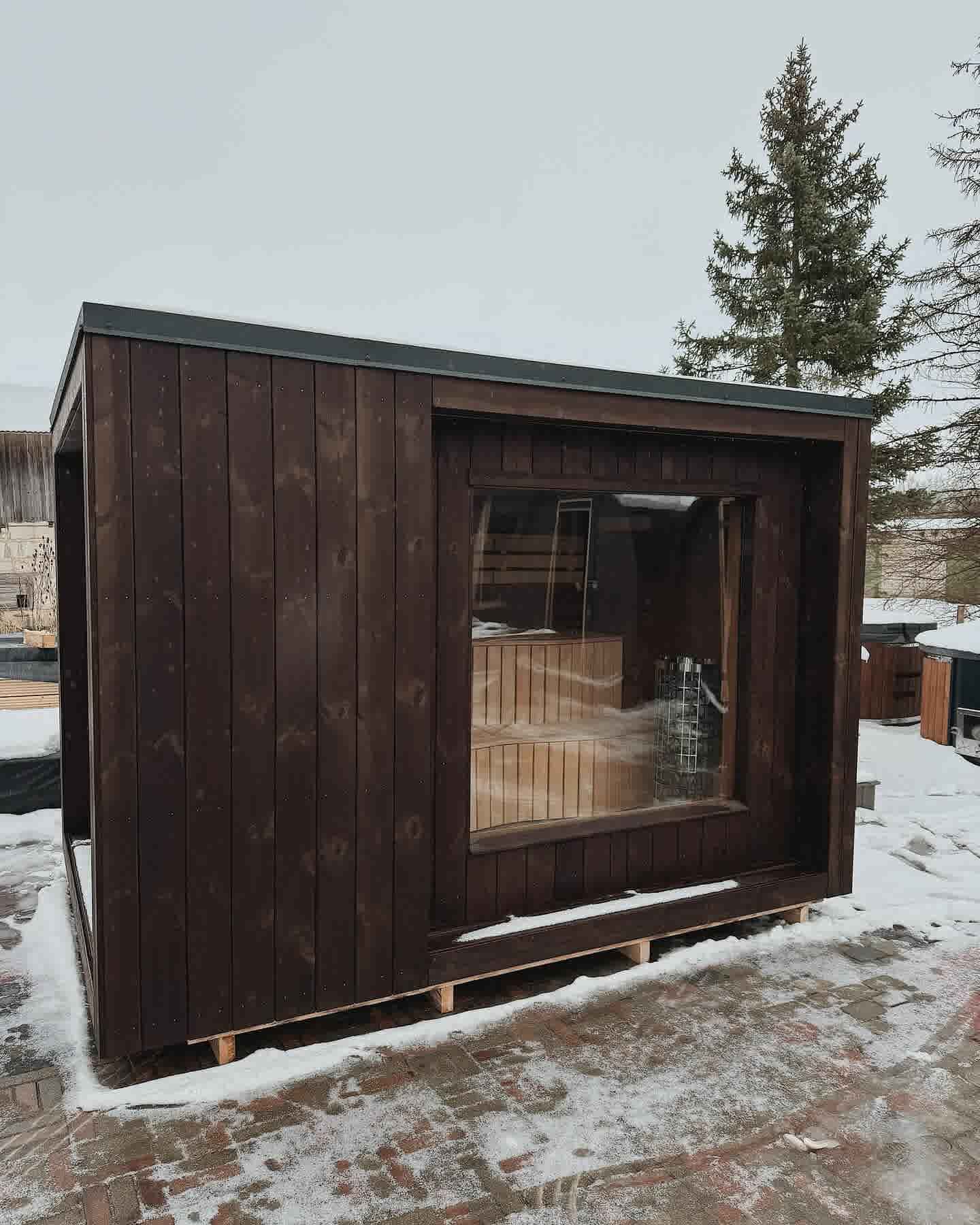 Exterior of The Cubus modern outdoor sauna in dark-stained timber with a large panoramic glass window.