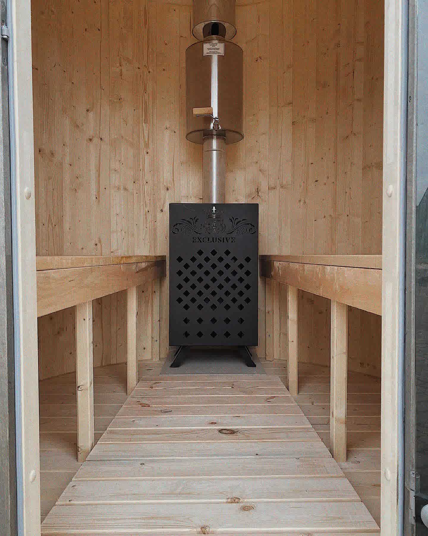 Detailed interior of The Cupa vertical sauna featuring a black exclusive wood-fired stove and symmetrical benches.